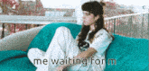 a woman is sitting on a blue couch with the words `` me waiting for m '' written below her .
