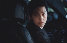a man in a suit sits in the driver 's seat of a car holding a gun
