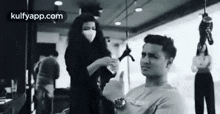 a man is getting his hair cut by a woman wearing a face mask .