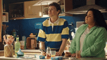 a woman in a green shirt stands next to a man in a blue and yellow striped shirt
