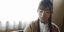a young woman is sitting in a chair in front of a window . she is wearing a sweater and a white shirt .
