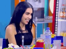 a woman in a black dress sits at a table with a plate of food and drinks