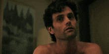 a shirtless man looks at the camera with a painting behind him