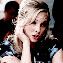 a woman in a plaid shirt is sitting at a table with her hand on her chin