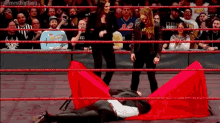 a wrestler is laying on the ground in a wrestling ring while a crowd watches .