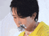 a man wearing a yellow shirt and a pearl necklace holds a flower in his mouth