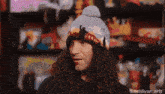 a man with long curly hair wearing a beanie with a picture of a building on it