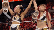 two female wrestlers are holding up their championship belts