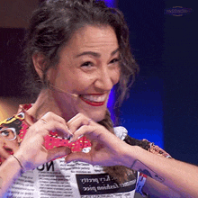 a woman making a heart shape with her hands while wearing a newspaper shirt with the word passmore on it