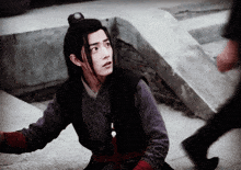 a man with long black hair is sitting on the ground looking at the camera