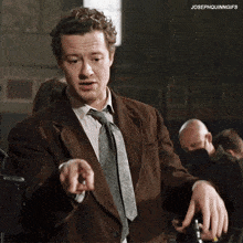 a man in a suit and tie is standing in front of a sign that says josephquinngifs on it