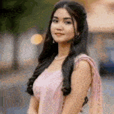 a woman in a pink dress and a pearl necklace is standing in front of a blurry background .