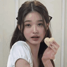 a young woman is holding a heart shaped cookie in her hand and looking at the camera .