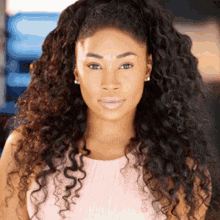 a woman with curly hair is wearing a pink top and earrings