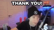 a man wearing a black beanie is sitting in front of a microphone and says `` thank you '' .