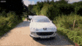 a white peugeot car is driving down a road with trees on the side