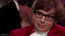 a man wearing glasses and a red jacket is asking come again ?