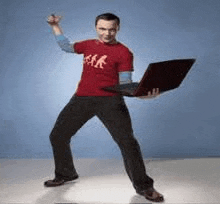 a man in a red shirt is holding a laptop computer while standing on one leg .