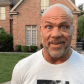 a bald man with a beard is standing in front of a brick house .
