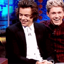 two young men are sitting next to each other and smiling .