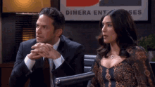a man and a woman are sitting in front of a dimera enterprise sign