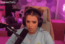 a woman wearing headphones and a necklace is sitting in front of a microphone with the words sweettails written above her