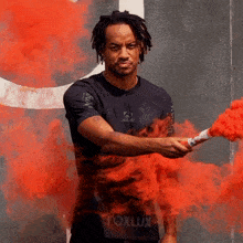 a man in a foxlux shirt holds a red smoke bomb in his hand