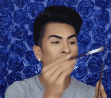 a man is applying makeup to his face in front of a wall of blue roses
