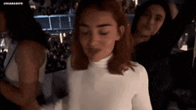 a woman in a white turtleneck is dancing with other women in a dark room .