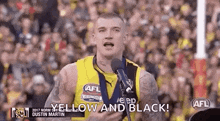 a man in a yellow and black jersey is standing in front of a microphone and speaking into it .
