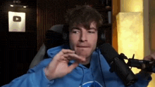 a man wearing headphones and a blue hoodie is sitting in front of a microphone in a room .