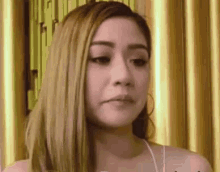a woman with long blonde hair is making a funny face in front of a curtain .