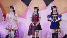 three girls are standing next to each other on a stage and one of them is wearing a blue top with a x on it
