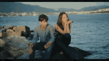 a man and a woman sit on a rock near the water