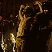 a man without a shirt is singing into a microphone while another man stands behind him