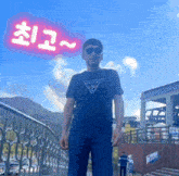 a man wearing a guess shirt and sunglasses stands in front of a fence