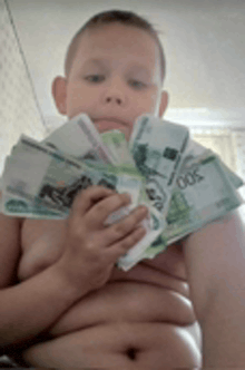 a shirtless boy is holding a bunch of money in front of his face .