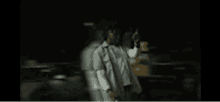 a man in a white jacket is standing in a dark room holding a tablet .