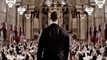 a man in a suit is standing in front of a large crowd of people in a large room .