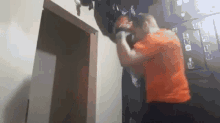 a man in an orange shirt is standing in a room with a door .