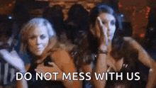 a couple of women standing next to each other in a club with the words `` do not mess with us '' written on the screen .