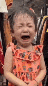 a little girl in a pink dress is crying in front of a rack of clothes .