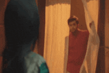 a man in a red shirt is looking out of a window at a woman in a green dress .