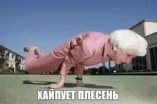 an elderly woman in a pink suit is doing push ups on a green lawn .