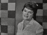 a woman stands in front of a checkered wall and smiles