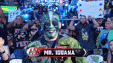a man with green paint on his face and a sign that says mr. iguana in front of a crowd