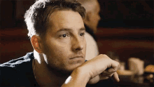 a man is sitting at a table with his hand on his chin and looking at something .