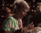 a woman in a green and white polka dot shirt is sitting at a table with a plate of food