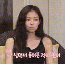 a woman in a black tank top is sitting on a couch and making a funny face in korean .