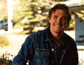 a young man wearing a denim jacket is smiling for the camera .